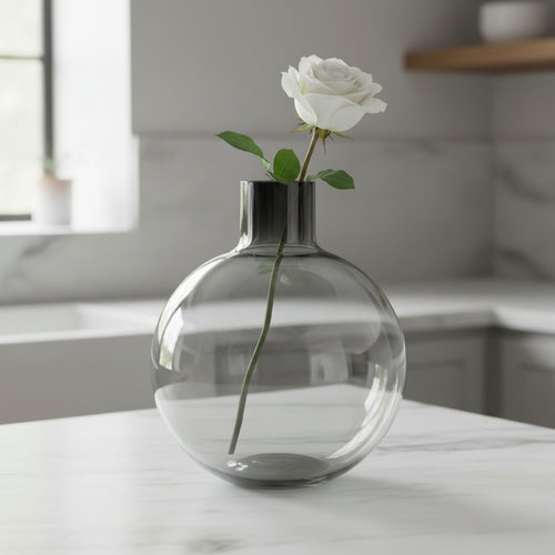 Smoked grey glass bottle vase holding a single white rose on a marble kitchen counter