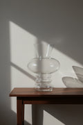 Clear stacked bubble glass vase on a dark walnut console in raking daylight