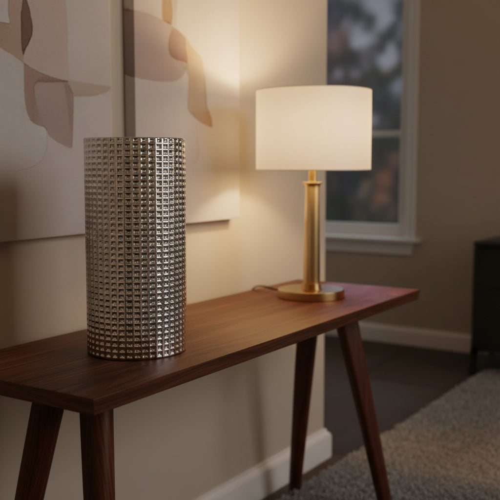 Clear glass vase with raised silver dots on a walnut console beside a lit brass lamp
