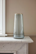 Smoked grey glass vase with a gold rim on a pale marble mantelpiece