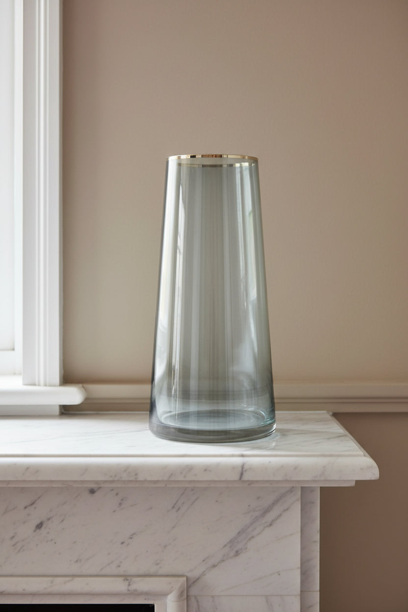 Smoked grey glass vase with a gold rim on a pale marble mantelpiece