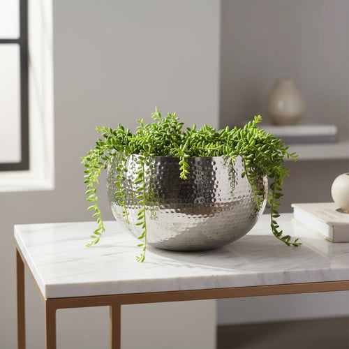Hammered silver bowl planter with trailing greenery on a marble console table