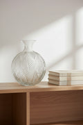 Clear pressed fern glass vase on a pale oak shelf beside a stack of books
