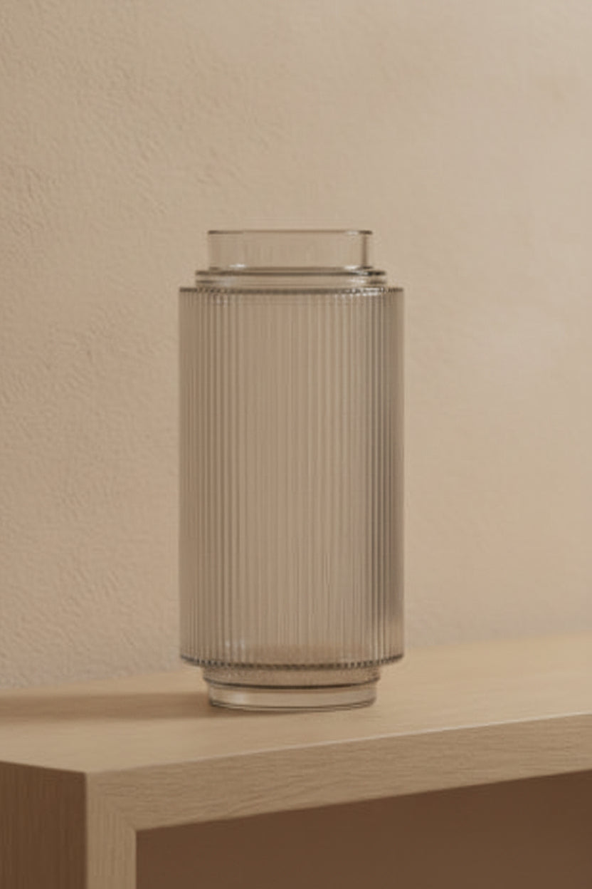 Clear ribbed glass vase on a pale oak console table against a plaster wall