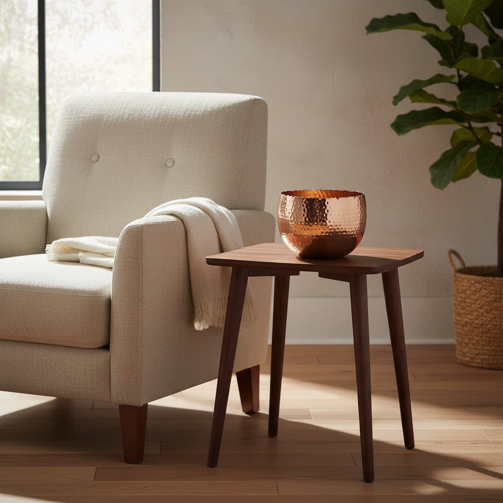 Hammered copper planter on a walnut side table beside a linen armchair