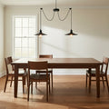 Two-head black pendant hanging from a white ceiling above a walnut dining table with chairs, in a bright calm dining room