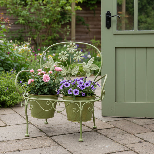 Sage green bench plant stand holding two flowering pots on a stone patio beside a garden door