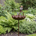 Rusted scalloped bird bath on its stand in a green garden border