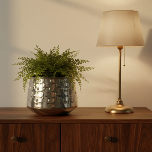 Beaten silver planter holding a fern on a walnut console beside a lit brass lamp
